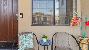 Ein Zimmer mit Holztür, einem Fenster mit Blick auf Gebäude, zwei Korbstühle, einem kleinen Tisch mit Pflanze und einer dekorativen Vase mit Blumen.