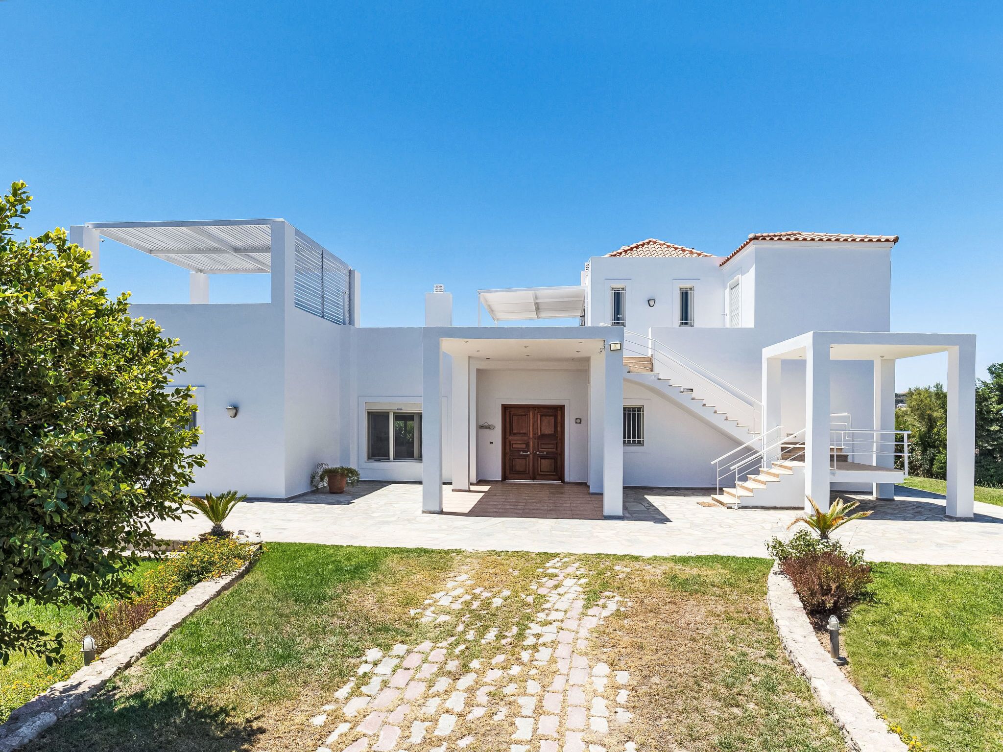 A modern two-story house with a covered entrance, a staircase, and a paved driveway.