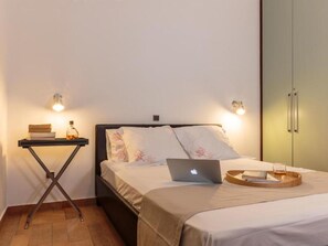 A bedroom with a bed, a laptop, a tray with a glass, and a nightstand with books and a bottle. - Belvedere Beachfront by Interhome (Kolympia)
