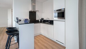 A modern kitchen with white cabinetry, a stainless steel range hood, a built-in oven, and a black countertop. - 4-guest Apartment in Breskens (Breskens)