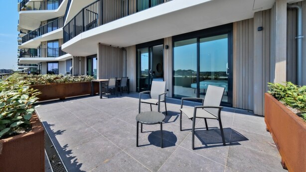 A modern outdoor seating area with chairs and tables, surrounded by large windows and balconies. - Coastal Apartment Stay in Breskens (Breskens)
