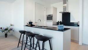 A modern kitchen with a central island, bar stools, a sink, and a stainless steel range hood. - Coastal Apartment Stay in Breskens (Breskens)