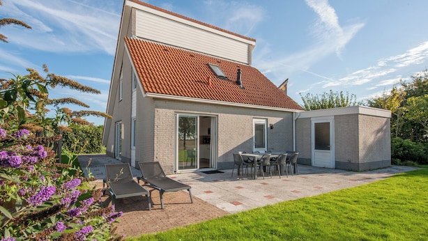 A modern two-story house with a tiled roof, a patio with a table and chairs, and a small garden area with purple flowers. - Scharendijke Stay With Private Sauna (Scharendijke)