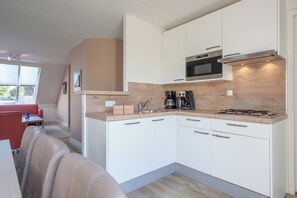 A compact kitchen with white cabinets, a microwave, a gas stove, and a coffee maker. - Scharendijke Stay With Private Sauna (Scharendijke)