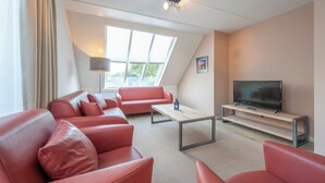 A modern living room with a sofa set, a coffee table, a television on a stand, and a large window with a view of greenery. - Scharendijke Stay With Private Sauna (Scharendijke)