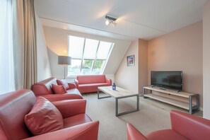 A modern living room with a sofa set, a coffee table, a television on a stand, and a large window with a view of greenery. - Scharendijke Stay With Private Sauna (Scharendijke)