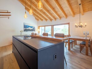 A modern kitchen with a central island, wooden ceiling beams, and a dining area with a chandelier. - Miraselva 1.7 by Interhome (Flims)