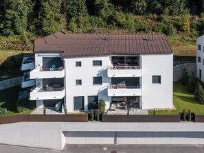 Ein mehrgeschossiges Wohngebäude mit Balkonen, einer flachen Dachterrasse und einer umlaufenden Grünanlage.
