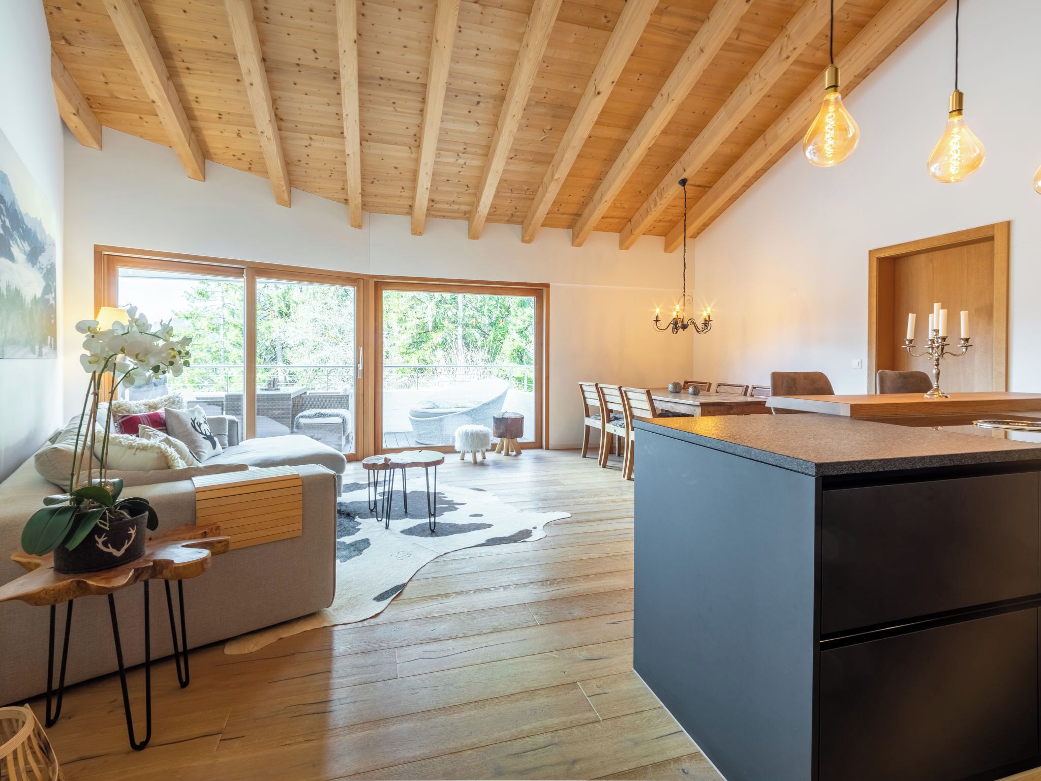 A modern kitchen with a central island, wooden beams on the ceiling, and a dining area with a chandelier.