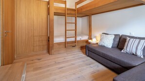 Ein Stockbett mit einer Leiter, ein Holzschrank, ein Sofa und ein kleiner Nachttisch mit Lampe.