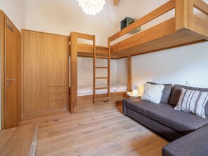 Ein Stockbett mit einer Leiter, ein Holzschrank, ein Sofa und ein kleiner Nachttisch mit Lampe.