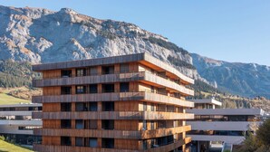 Ein mehrstöckiges Gebäude mit Holzfassade vor einer gebirgigen Landschaft.