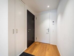 Um corredor com piso de madeira, uma porta preta e uma porta branca com painel de controle.