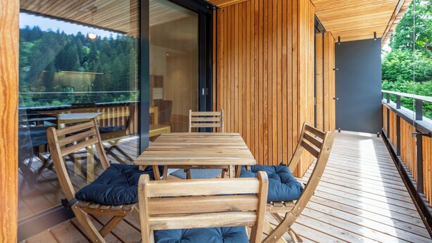 Eine Holzterrasse mit Tisch und Stühlen mit Blick auf eine bewaldete Landschaft.