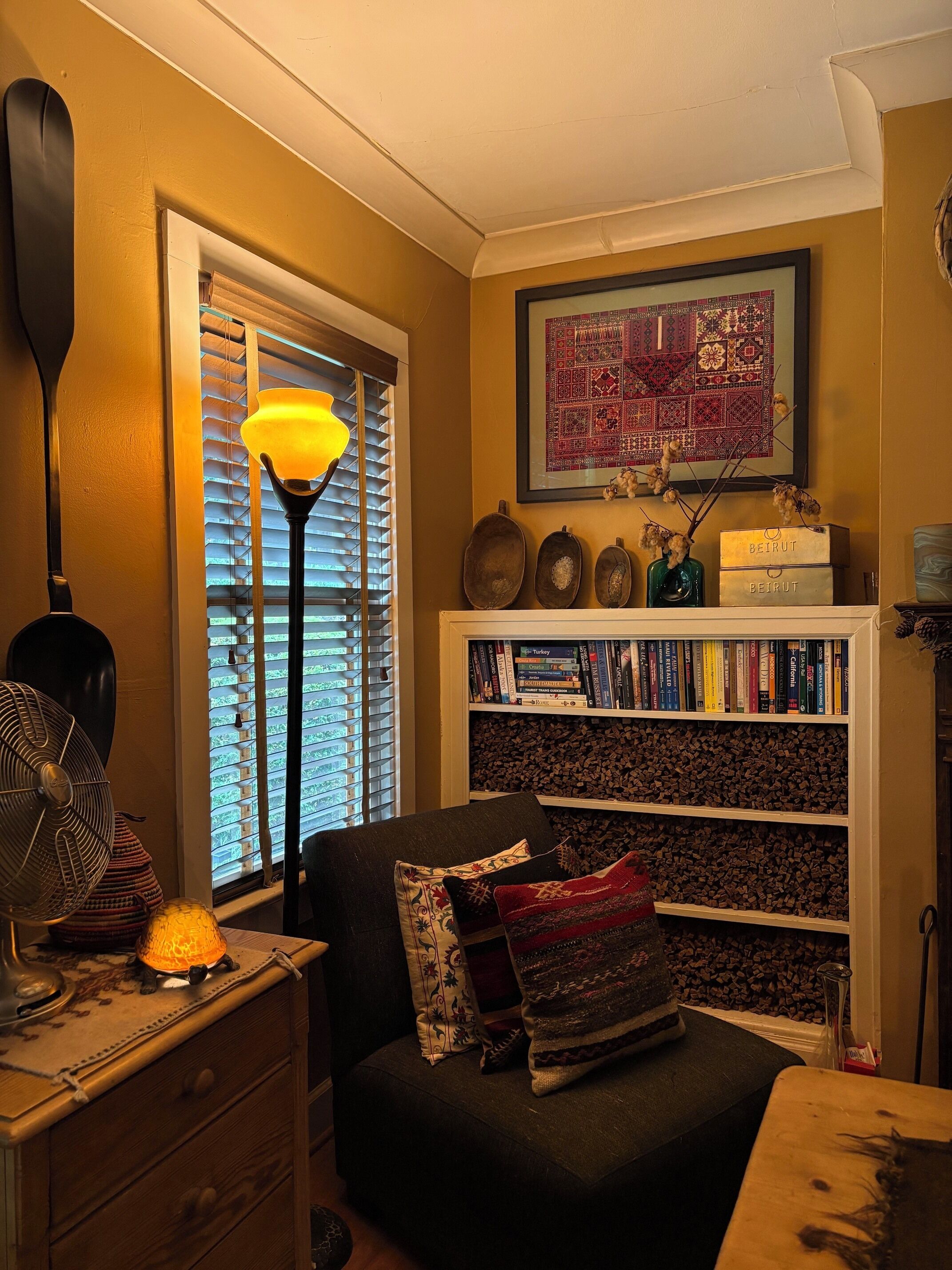 A cozy reading nook with a bookshelf, a lamp, and a window with blinds.