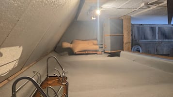 A room with a sloped ceiling, a wooden chair, a metal chair, and a suitcase.