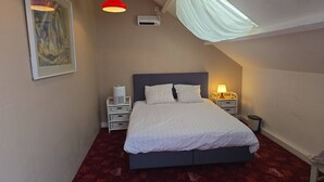 Un dormitorio con cama, mesitas de noche, un calefactor en la pared y una lámpara en el techo.
