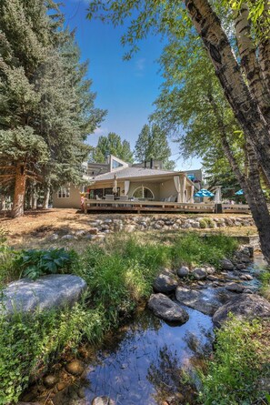 A house with a deck, surrounded by trees and a small stream. - Eagle-Vail Duplex - Golf Front - Near Beaver Creek (Avon)