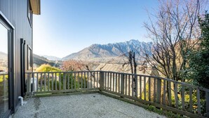 A balcony with a view of mountains, a wooden fence, and a building with a window. - Mountain View Marina with Remarkables Backdrop (Queenstown)