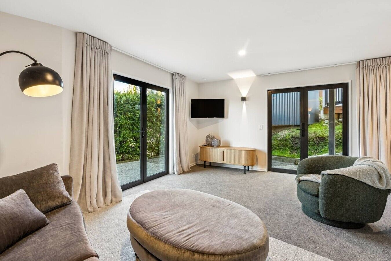 A modern living room with a sofa, ottoman, and armchair, a flat-screen TV, and a cabinet.