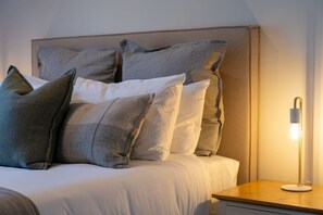 Ein ordentlich bezogenes Bett mit vielen Kissen und einer Nachttischlampe.