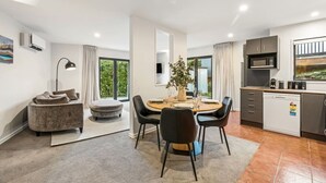 A modern living room with a dining area, a kitchen, and a view of greenery. - Mountain View Marina with Remarkables Backdrop (Queenstown)
