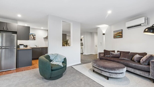 A modern living space with a kitchen, a green armchair, a grey sofa, and a large mirror. - Mountain View Marina with Remarkables Backdrop (Queenstown)