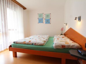 A single-bed room with a wooden headboard, a green bedspread, and two pillows. There is a small table with a remote control on it, and a wall-mounted lamp. - GOLF Apartments Appartement/Fewo 2-Bettwohnung Nr. 4 by Interhome (Saas-Fee)