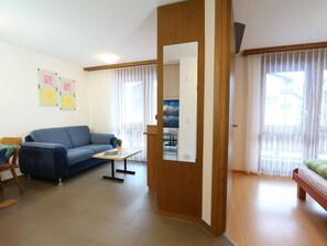 A living room with a sofa, a coffee table, and a wooden door leading to a kitchen. - GOLF Apartments Appartement/Fewo 2-Bettwohnung Nr. 4 by Interhome (Saas-Fee)