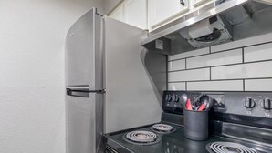 Eine Küche mit einem Edelstahlkühlschrank, einem schwarzen Herd mit vier Kochfeldern und einem schwarzen Topf mit Kochgeschirr auf dem Herd.