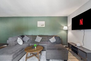 A living room with a sectional sofa, a coffee table, a TV mounted on the wall, and a lamp. - 2 Min AT&T Stadium Walk | Cozy & Clean 2BR Apt (Arlington)