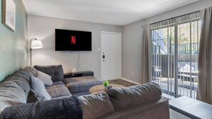 Ein Wohnzimmer mit einer Couch, einem an der Wand montierten Fernseher und einer Glastür zum Außenbereich.