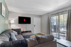 Ein Wohnzimmer mit einer Couch, einem an der Wand montierten Fernseher und einer Glastür zum Außenbereich.