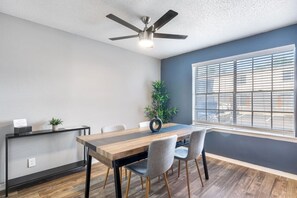 A conference room with a wooden table, grey chairs, a ceiling fan, and a window with blinds. - 2 Min AT&T Stadium Walk | Cozy & Clean 2BR Apt (Arlington)