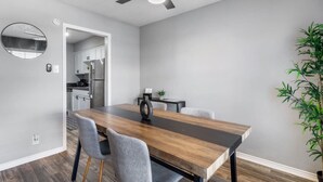 A dining area with a wooden table, grey chairs, a ceiling fan, and a potted plant. - Arlington 2BR | AT&T, Globe Life, 6 Flags, Parking (Arlington)