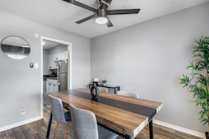 A dining area with a wooden table, grey chairs, a ceiling fan, and a potted plant. - Arlington 2BR | AT&T, Globe Life, 6 Flags, Parking (Arlington)