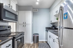 A modern kitchen with stainless steel appliances, white cabinetry, and a patterned rug. - Arlington 2BR | AT&T, Globe Life, 6 Flags, Parking (Arlington)