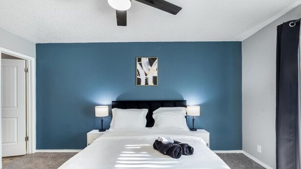 A bedroom with a bed, two bedside lamps, a ceiling fan, and a door. - Arlington 2BR | AT&T, Globe Life, 6 Flags, Parking (Arlington)