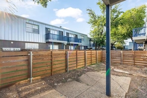 A residential building with a wooden fence, a paved area, and a clear sky. - Arlington 2BR | AT&T, Globe Life, 6 Flags, Parking (Arlington)