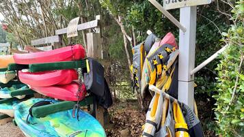 Une collection de kayaks et de gilets de sauvetage est suspendue à un porte-équipement, avec une pancarte indiquant « Gilets de sauvetage » au-dessus.