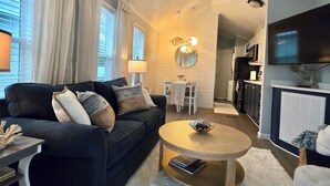 A modern living room with a dark sofa, a round coffee table, and a dining area in the background. - Lakeside Oasis Lake Norman Tiny Home 
Pool, Kayaks & Pickleball (Sherrills Ford)