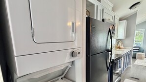 A compact kitchen with a built-in washer and dryer, a black refrigerator, and white cabinetry. - Lakeside Oasis Lake Norman Tiny Home 
Pool, Kayaks & Pickleball (Sherrills Ford)