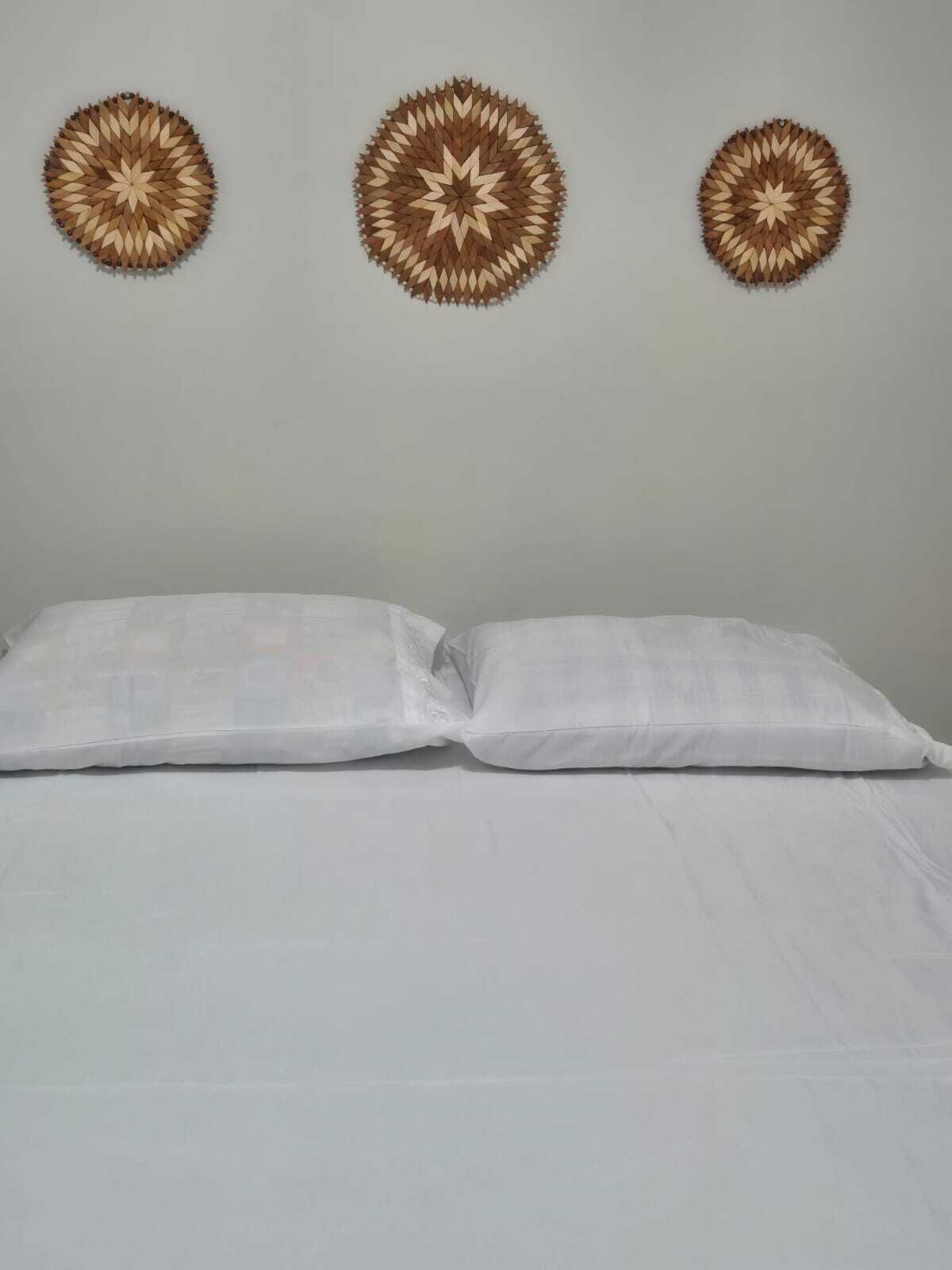 Un letto con biancheria bianca e due cuscini, una parete spoglia e tre decorazioni circolari a parete.