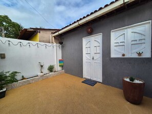 A house with a grey exterior, a white door, and a white window. There is a small garden with plants and a large planter. - Casa Kairós | Comfort 500 m from the Beach in São Miguel dos Milagres (São Miguel dos Milagres)