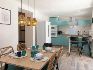 Eine moderne Küche mit türkis-blauen Schränken, einem weißen Kühlschrank und einem Essbereich mit einem Holztisch, gedeckt für vier Personen.