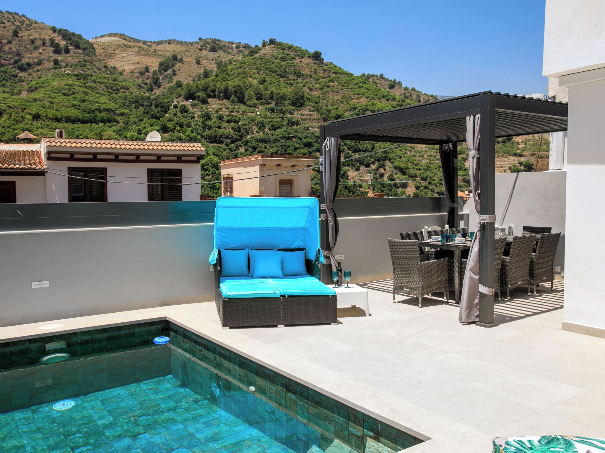 Area piscina sul tetto con una poltrona blu, un tavolino con sedie e un pergolato.