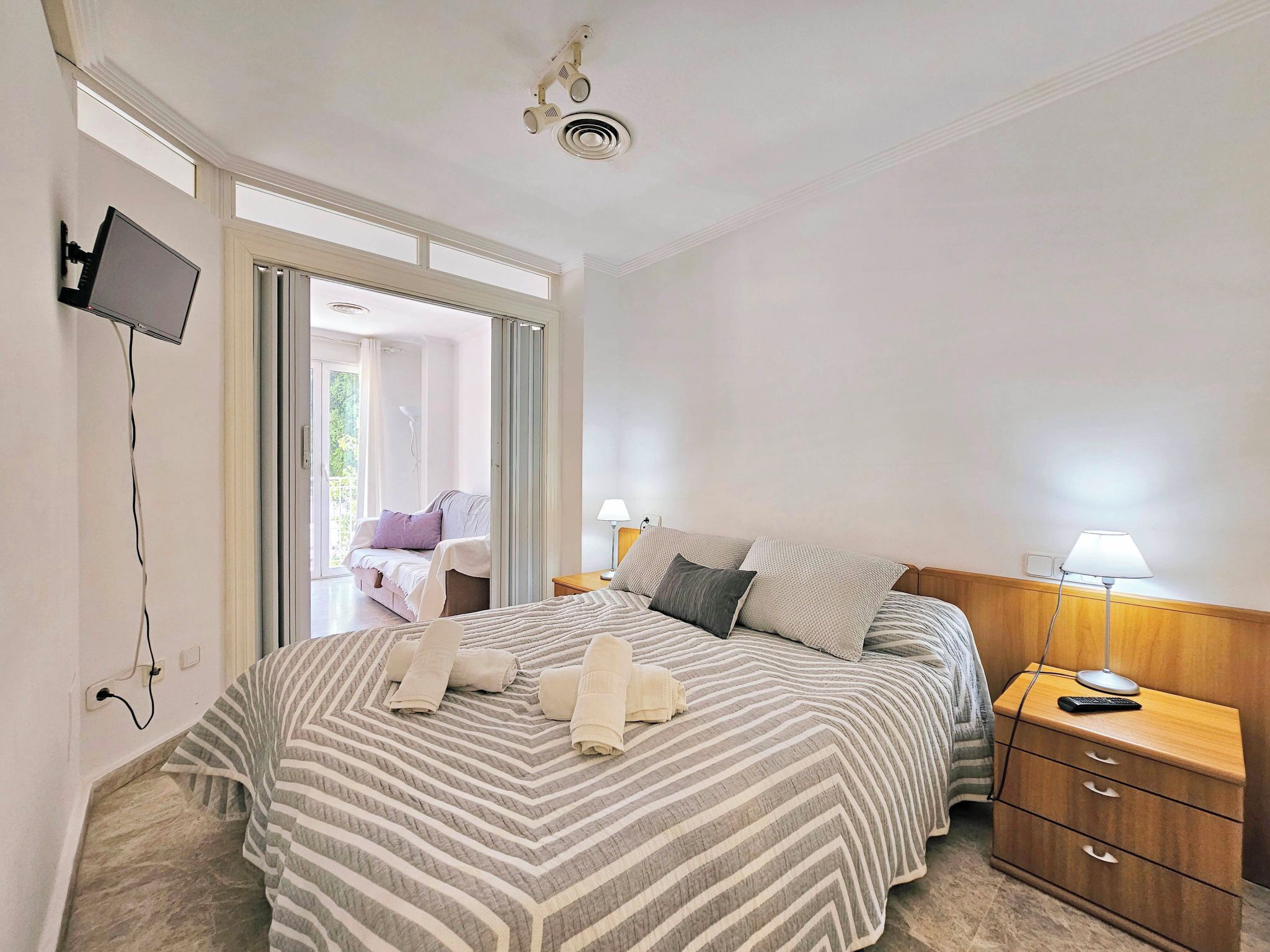 A hotel room with a bed, bedside table, lamp, and a TV mounted on the wall.