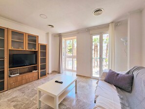 A living room with a TV, a white coffee table, a sofa, and a sliding glass door leading to an outdoor area. - Apartamento Alba 1 by Interhome (Cartagena)