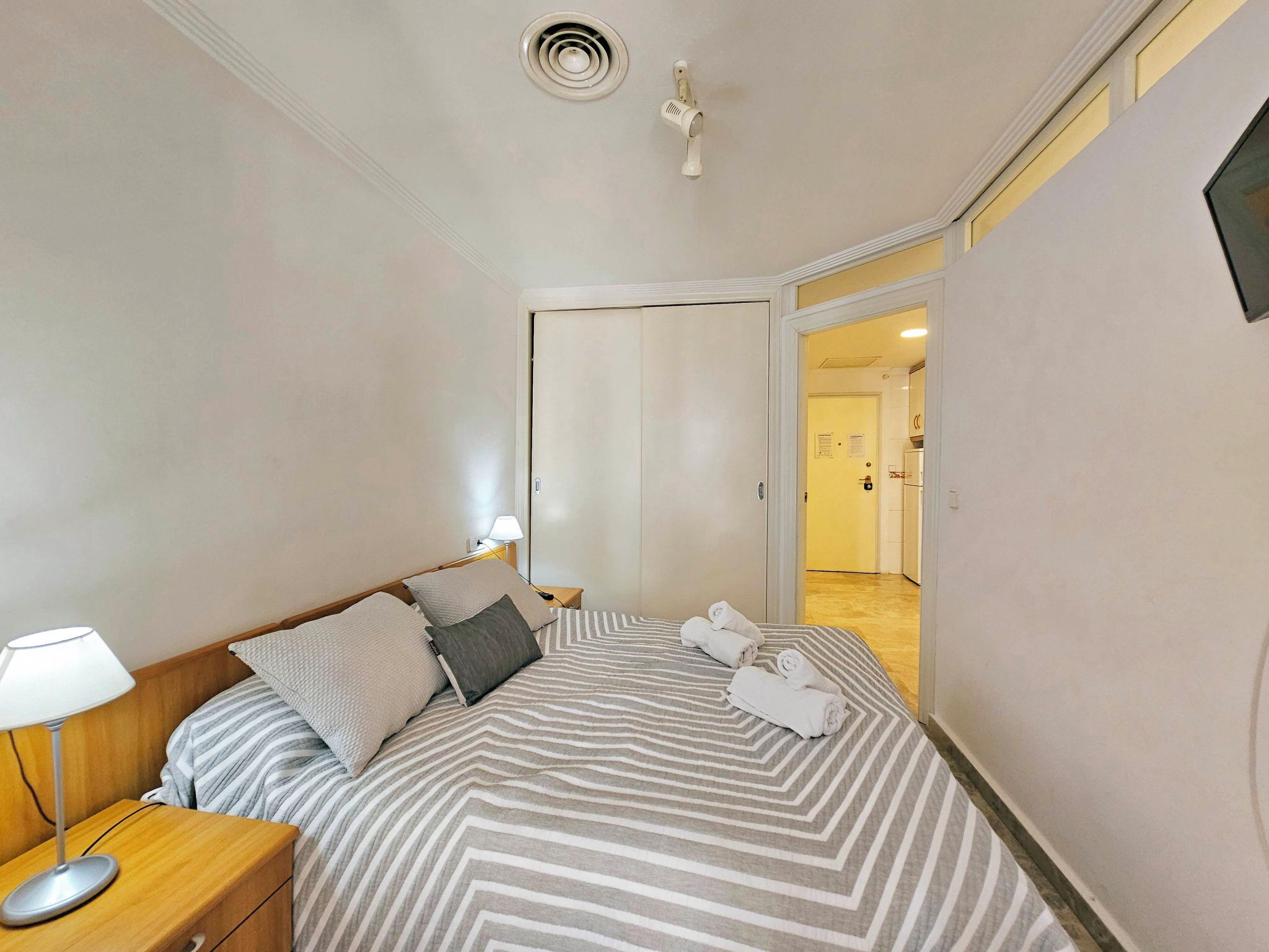 Ein Schlafzimmer mit Bett, Nachttisch, Lampe und Blick in die Diele.