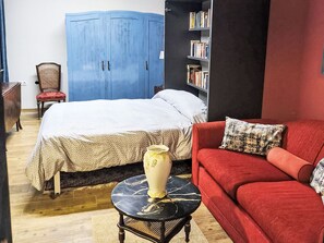 Ein Zimmer mit einem Bett, einem roten Sofa, einem Bücherregal und einem blauen Kleiderschrank.